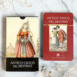 May include: Two decks of cards, one in a black box and the other in a red box. The black box features a woman in a historical dress, and the red box shows a couple. Both boxes have the text "ANTICO GIOCO DEL DESTINO".