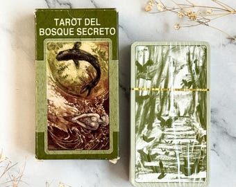 May include: A tarot card deck and box set with the text "TAROT DEL BOSQUE SECRETO" in green and white. The box features an illustration of a whale and figures. The deck has a green and white forest design.