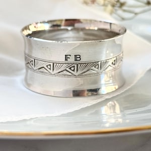 May include: Silver napkin ring with a geometric design and the initials "FB" engraved on the side.