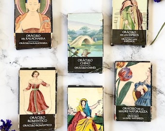 May include: A collection of six oracle card decks with colorful illustrations and text in Spanish and Portuguese. The decks include the Oracle of the Kalachakra, the Oracle of the Mirrors, the Chinese Oracle, the Romantic Oracle, the Oracle of the Danube, and the Oracle of Mother Nature.