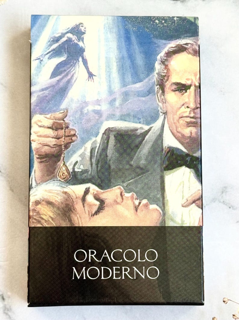 May include: A tarot card deck box featuring a vintage illustration. The artwork depicts a man holding a pendulum over a woman, with a floating figure in the background. The text "ORACLO MODERNO" is printed on the bottom.