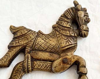 May include: A detailed, antique-style brass horse figurine. The horse is in a running pose, with intricate etched patterns on its body, saddle, and bridle. The brass has a warm, aged patina, giving it a vintage appearance.