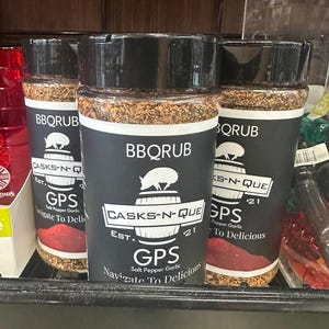 May include: Three glass jars of BBQ rub with black lids and labels. The labels have a pig and a barrel logo with the text "Casks-N-Que Est. '21 GPS Salt Pepper Garlic Navigate To Delicious" on the front.