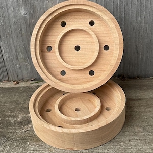 May include: Two wooden round cake molds with a center hole and multiple smaller holes around the edge. The molds are stacked on top of each other.