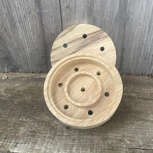 May include: A wooden round dish with a center circle and multiple holes around the edge. The dish is made of light brown wood and has a natural finish.