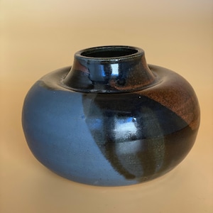 May include: A ceramic vase with a rounded body and a narrow neck. The vase has a colour-blocked design with shades of blue, brown, and black. The glossy finish adds a touch of elegance to this decorative piece.