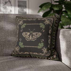 May include: A black throw pillow with a decorative border and a vintage illustration of a butterfly in the center. The butterfly is surrounded by green leaves and small brown dots.