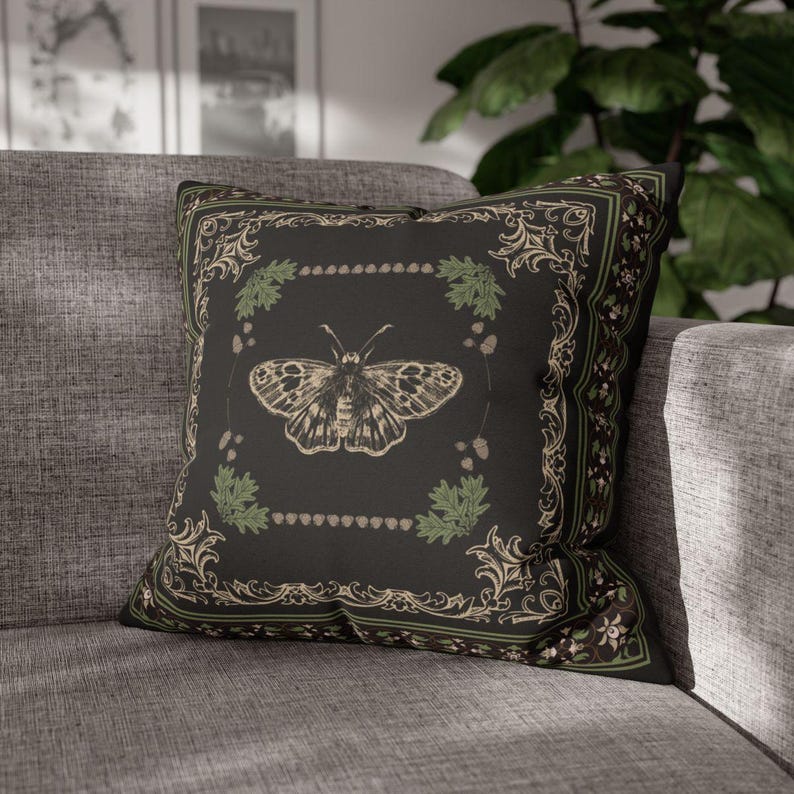 May include: A black throw pillow with a decorative border and a vintage illustration of a butterfly in the center. The butterfly is surrounded by green leaves and small brown dots.