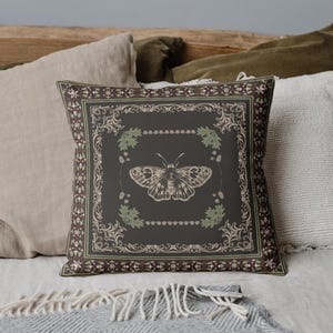 May include: A decorative throw pillow with a dark brown background featuring a detailed illustration of a butterfly surrounded by floral elements. The pillow has a black and white ornate border.