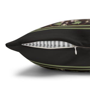 May include: A black pillow with a green and gold floral pattern. The pillow has a zipper closure and a white and gray striped lining.