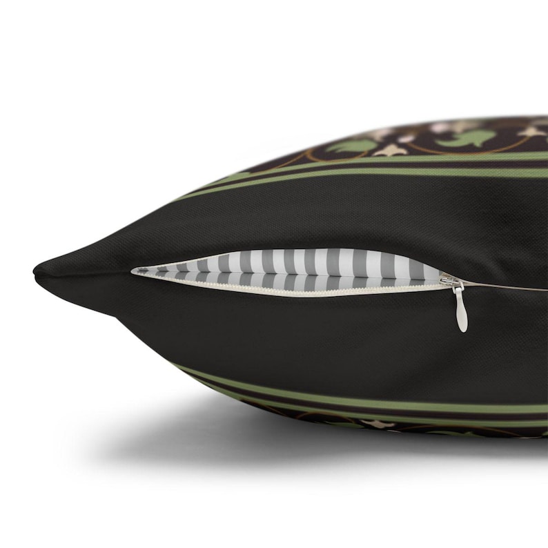 May include: A black pillow with a green and gold floral pattern. The pillow has a zipper closure and a white and gray striped lining.