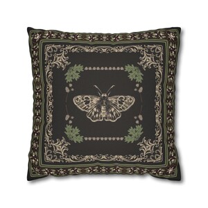 May include: A black throw pillow with a decorative border and a vintage illustration of a butterfly in the center. The butterfly is surrounded by a wreath of green leaves and brown berries.