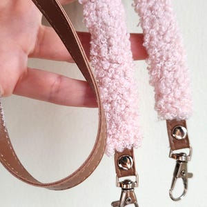 May include: A bag strap featuring a soft, light pink textured sherpa-style fabric section and a smooth brown faux leather section. The strap includes silver-toned metal swivel lobster clasps attached to the ends with small silver rivets.
