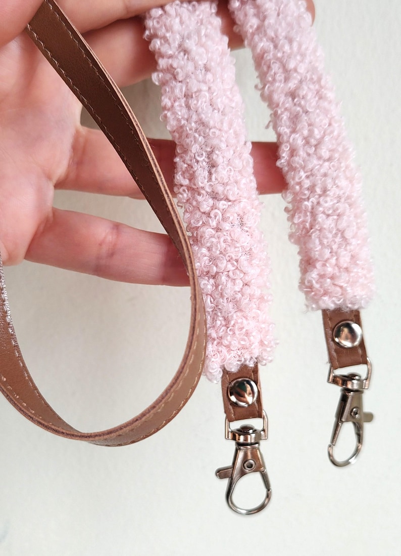 May include: A bag strap featuring a soft, light pink textured sherpa-style fabric section and a smooth brown faux leather section. The strap includes silver-toned metal swivel lobster clasps attached to the ends with small silver rivets.
