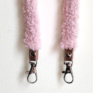 May include: A pair of light pink, textured, fuzzy sherpa-style straps featuring brown faux leather tabs secured with silver-tone metal snaps and finished with silver-tone swivel lobster claw clasps at the bottom ends for attachment.