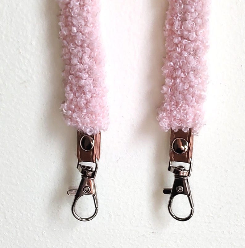 May include: A pair of light pink, textured, fuzzy sherpa-style straps featuring brown faux leather tabs secured with silver-tone metal snaps and finished with silver-tone swivel lobster claw clasps at the bottom ends for attachment.
