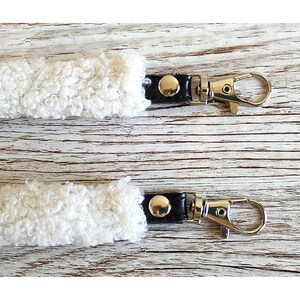 May include: Two white sherpa fleece straps featuring black leather-like connectors and silver-toned metal swivel lobster claw clasps. Each strap end is secured with a single silver-toned metal rivet, providing a functional attachment point.