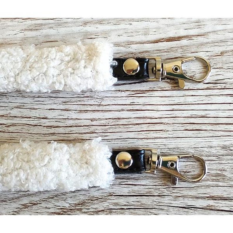 May include: Two white sherpa fleece straps featuring black leather-like connectors and silver-toned metal swivel lobster claw clasps. Each strap end is secured with a single silver-toned metal rivet, providing a functional attachment point.
