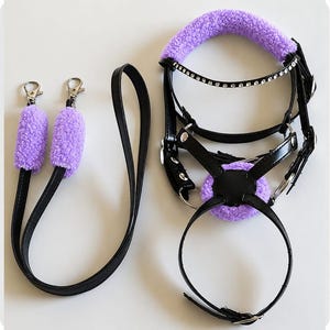 May include: A black leather horse bridle and matching lead rope set featuring bright purple fuzzy fleece padding on the noseband, crown piece, and lead clips. The bridle includes a browband adorned with a row of clear, sparkling rhinestones.