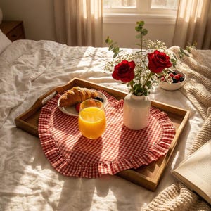 Puede incluir: Una bandeja de desayuno de madera sobre una cama, con un mantel individual a cuadros rojos y blancos. La bandeja contiene un cruas&aacute;n, fruta, un vaso de zumo de naranja, un jarr&oacute;n blanco con rosas rojas y un cuenco de bayas.