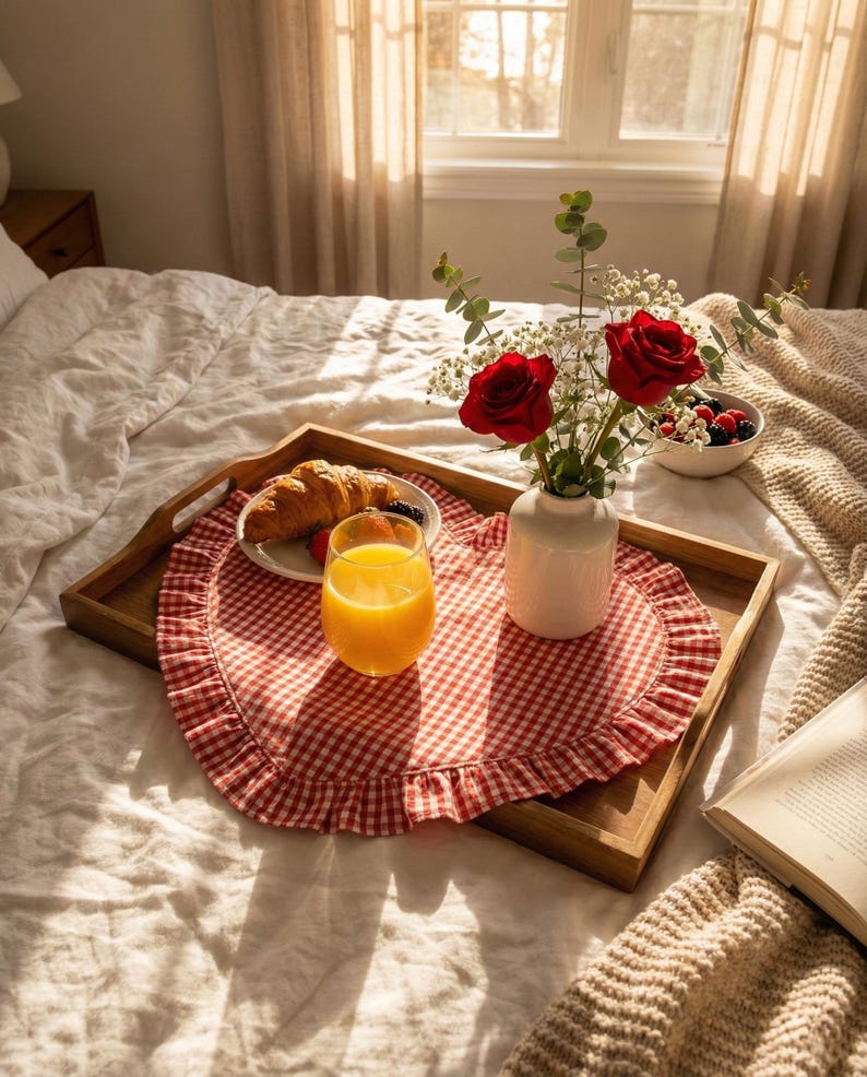 Puede incluir: Una bandeja de desayuno de madera sobre una cama, con un mantel individual a cuadros rojos y blancos. La bandeja contiene un cruas&aacute;n, fruta, un vaso de zumo de naranja, un jarr&oacute;n blanco con rosas rojas y un cuenco de bayas.
