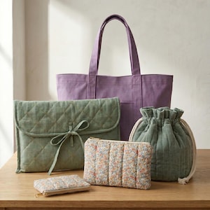 Può includere: Una collezione di borse che include una grande borsa tote in tela viola, una pochette a busta trapuntata verde salvia con chiusura a laccio, una borsa a sacco trapuntata verde salvia con cordini e due astucci rettangolari a fiori.