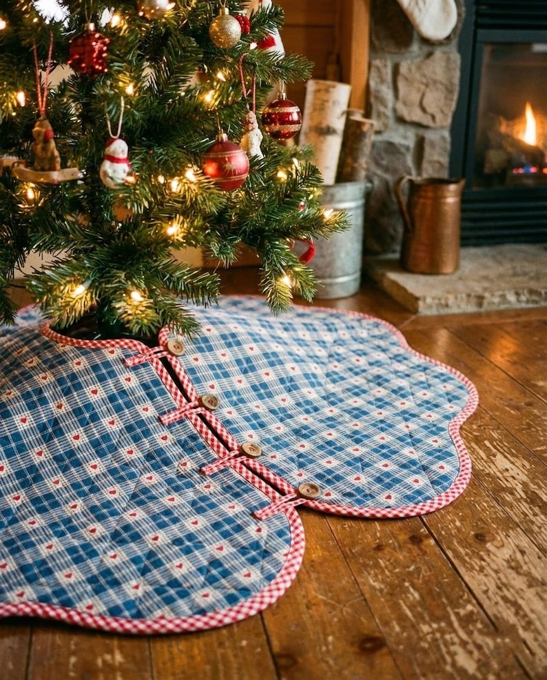 May include: A quilted Christmas tree skirt featuring a blue and white plaid pattern with small red hearts. The circular fabric mat has a scalloped edge trimmed in red and white gingham, secured with four wooden buttons and fabric loops.