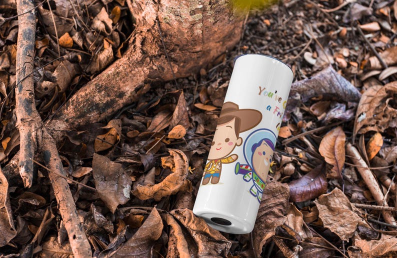 May include: White travel mug with a cartoon image of Woody and Buzz Lightyear from Toy Story. The mug has the text "You're a Friend to Me" printed on it.