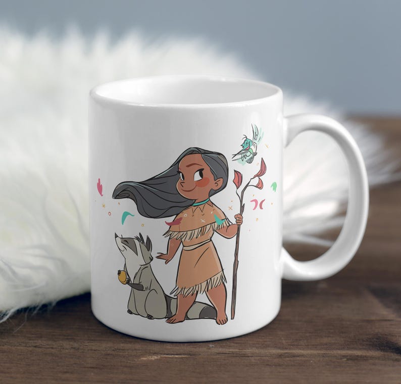May include: White ceramic mug with a cartoon illustration of a Native American girl with long black hair, wearing a brown dress and holding a stick with a bird on it. A raccoon is standing next to her. The mug has a white handle.