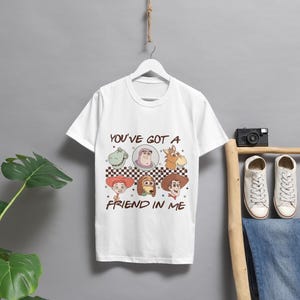 Op de afbeelding: Wit T-shirt met een grafische print van personages uit de Toy Story-filmfranchise. De grafiek toont Woody, Buzz Lightyear, Jessie, Rex en Slinky Dog. De tekst "You've got a friend in me" is onder de grafiek gedrukt.