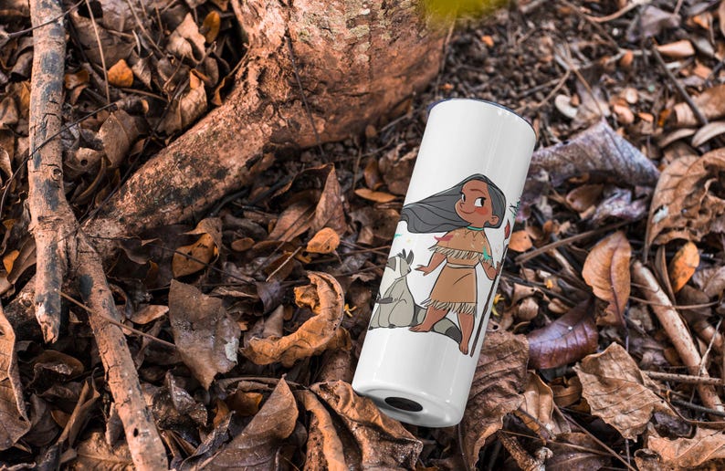 May include: White tumbler with a cartoon illustration of a Native American girl with long black hair, wearing a brown dress and holding a feather. Two white raccoons are beside her. The tumbler is on a bed of brown leaves.