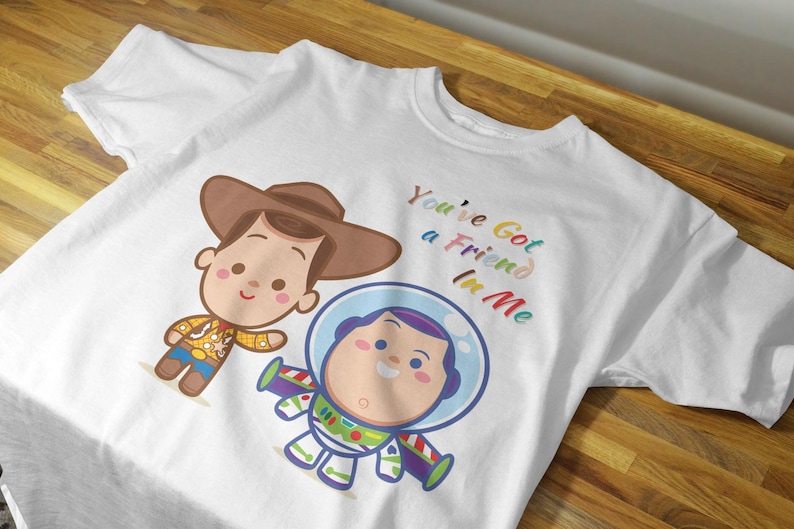 May include: White t-shirt with a cartoon image of Woody and Buzz Lightyear from Toy Story. The shirt has the text "You've Got a Friend in Me" printed on it in rainbow colors.