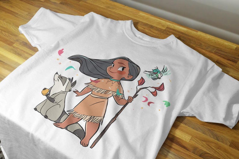 May include: White t-shirt with a cartoon illustration of a Native American girl with long black hair, wearing a brown dress and holding a stick. She is surrounded by a raccoon, a bird, and colorful flowers.