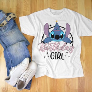 Op de afbeelding: Wit T-shirt met een blauw Stitch-personage dat een feestmuts draagt. De tekst "Birthday Girl" is in roze en zwart gedrukt.