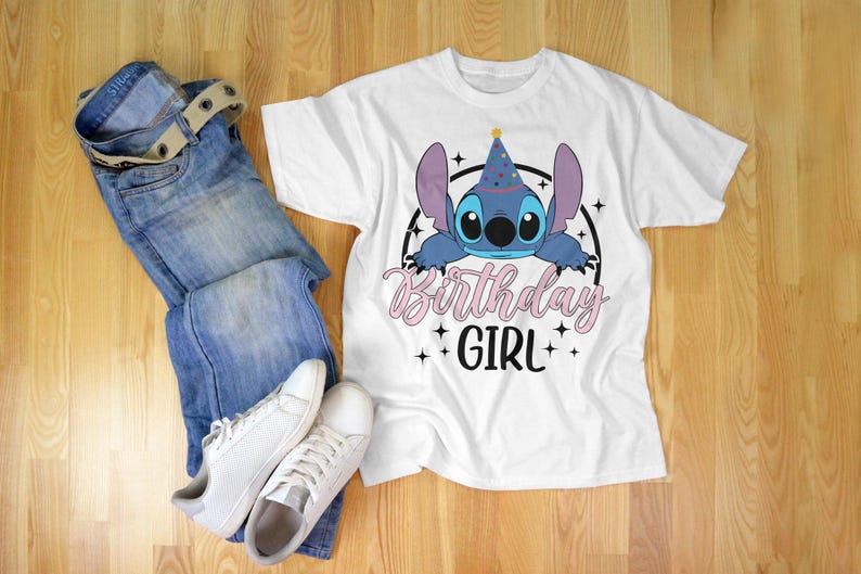 Op de afbeelding: Wit T-shirt met een blauw Stitch-personage dat een feestmuts draagt. De tekst "Birthday Girl" is in roze en zwart gedrukt.