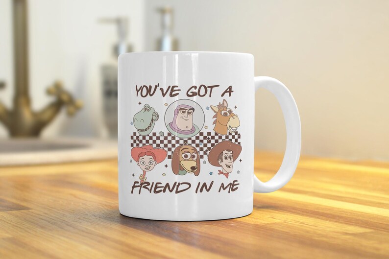 Op de afbeelding: Witte keramische mok met een kleurrijke illustratie van personages uit de Toy Story-franchise. De mok heeft een handvat en de tekst "You've got a friend in me" staat op de voorkant.