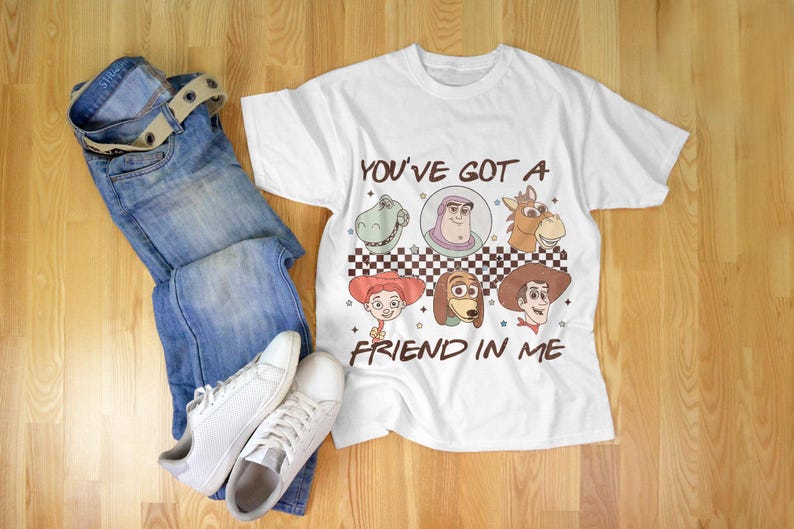 Op de afbeelding: Wit T-shirt met een cartoon afbeelding van personages uit de Toy Story film. Het shirt heeft de tekst "You've got a friend in me" erop gedrukt.