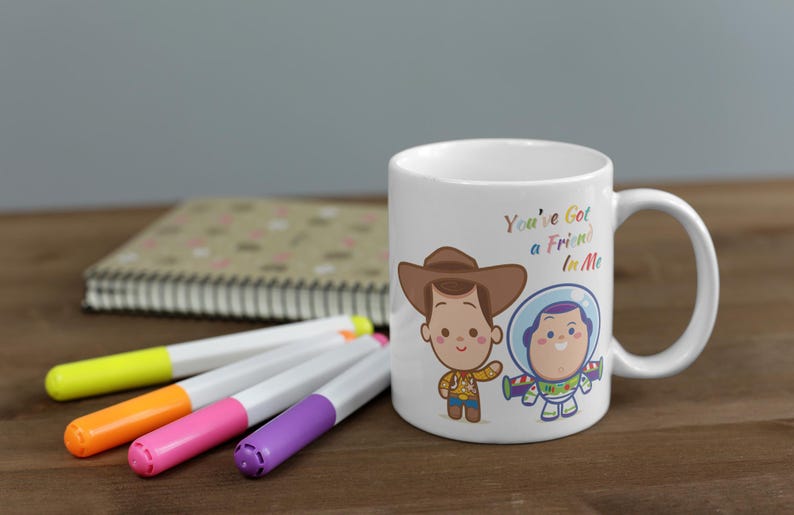 May include: White ceramic mug with a colorful cartoon image of Woody and Buzz Lightyear from Toy Story. The mug has the text "You've Got a Friend in Me" printed on it.