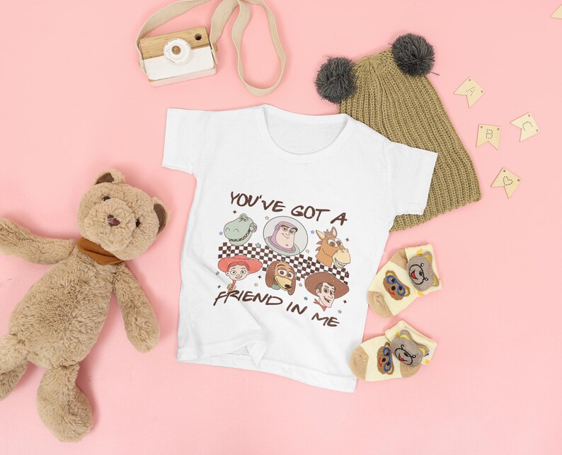 Op de afbeelding: Witte baby romper met een afbeelding van Toy Story-personages en de tekst "You've got a friend in me".