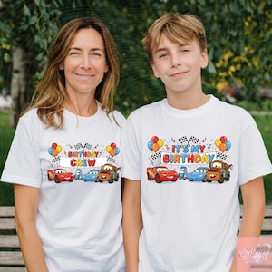 May include: Two white t-shirts with colorful graphics featuring cartoon cars, balloons, and checkered flags. One shirt says "BIRTHDAY CREW," the other says "IT'S MY BIRTHDAY." The shirts are worn by a woman and a boy.
