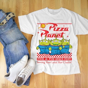 May include: White t-shirt with a graphic of three green aliens from the movie Toy Story. The graphic says "Pizza Planet" and "Food & Fun Space Port Serving Your Local Star Cluster!"