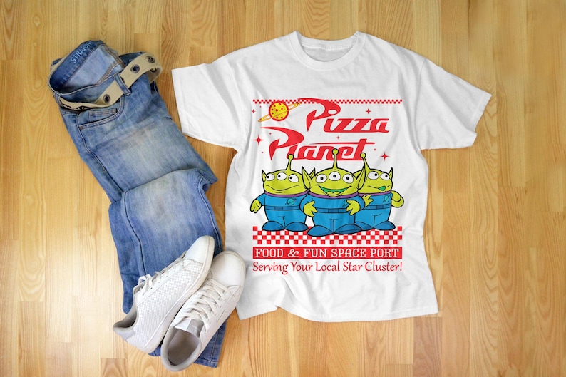 May include: White t-shirt with a graphic of three green aliens from the movie Toy Story. The graphic says "Pizza Planet" and "Food & Fun Space Port Serving Your Local Star Cluster!"