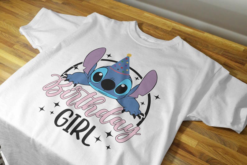 Op de afbeelding: Wit T-shirt met een blauw Stitch-personage dat een feestmuts draagt. De tekst "Birthday Girl" is geschreven in roze en zwart.