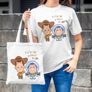 May include: White tote bag with a cartoon image of Woody and Buzz Lightyear from Toy Story. The bag has the text "You've Got a Friend in Me" printed on it.