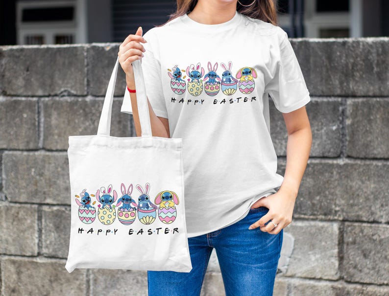 May include: White tote bag with a blue cartoon character holding an Easter egg. The bag has the text "Happy Easter" printed on it. A person is holding the bag and wearing a white t-shirt with the same design and the text "Happy Easter".