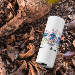 May include: White tumbler with a blue cartoon character holding an Easter egg. The text "Happy Easter" is printed on the tumbler.