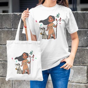 May include: White tote bag with a cartoon illustration of a Native American girl with long black hair, wearing a brown dress and holding a staff. She is accompanied by a raccoon. The bag has a white background with pink and blue floral accents.