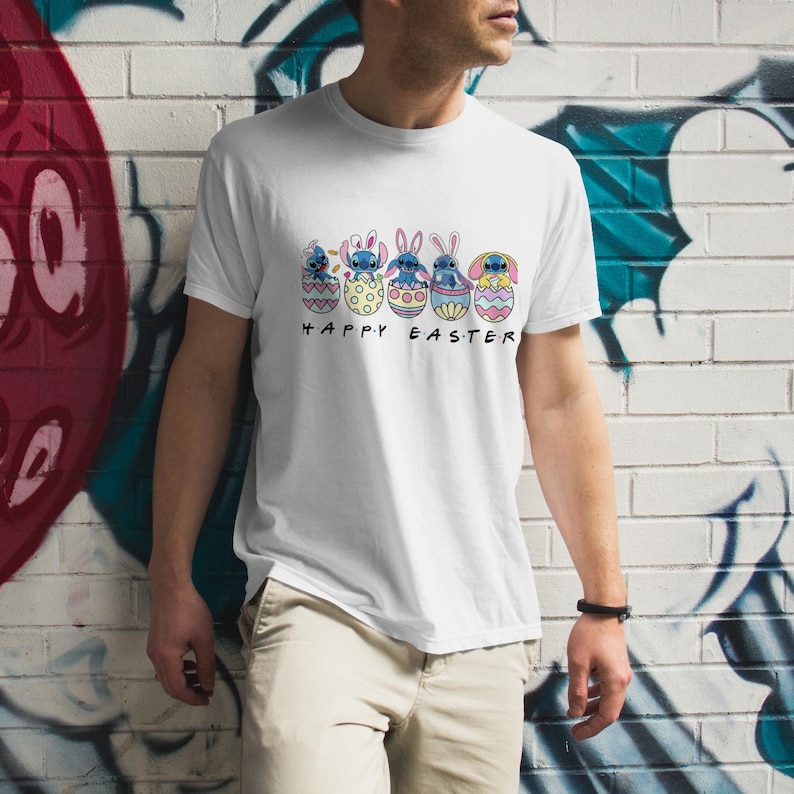 May include: White t-shirt with a graphic of five blue Stitch characters from the Disney movie Lilo & Stitch, each inside a colorful Easter egg. The text "Happy Easter" is printed below the eggs.