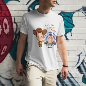 May include: White t-shirt with a cartoon image of Woody and Buzz Lightyear from Toy Story. The text "You've Got a Friend in Me" is printed on the shirt.