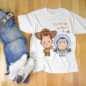May include: White t-shirt with a cartoon image of Woody and Buzz Lightyear from Toy Story. The shirt has the text "You've Got a Friend in Me" printed on it.
